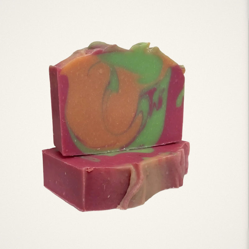 Two Apple Mango Tango goat milk soap bars with pink, orange and green swirls on a white background