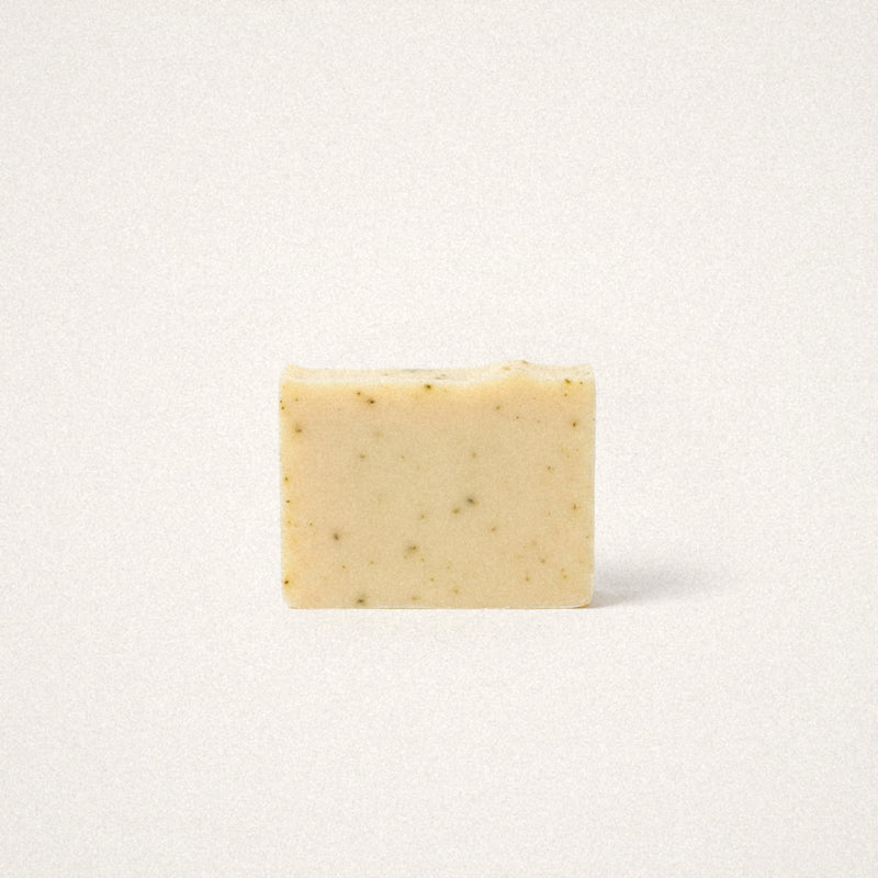 Lemongrass Sage goat milk soap bar, pale yellow with green herb flecks, on a white background