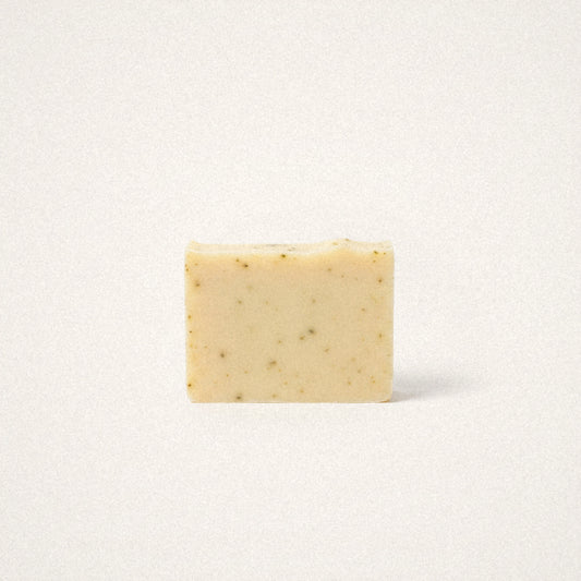 Lemongrass Sage goat milk soap bar, pale yellow with green herb flecks, on a white background