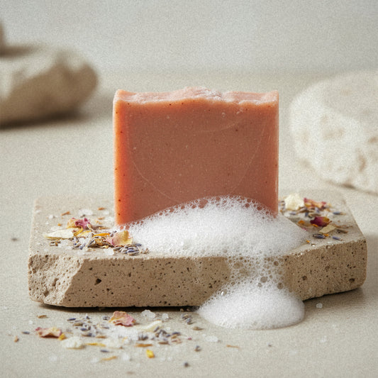 Sea Salt Blossom goat milk soap on a stone slab with lather and dried flower petals