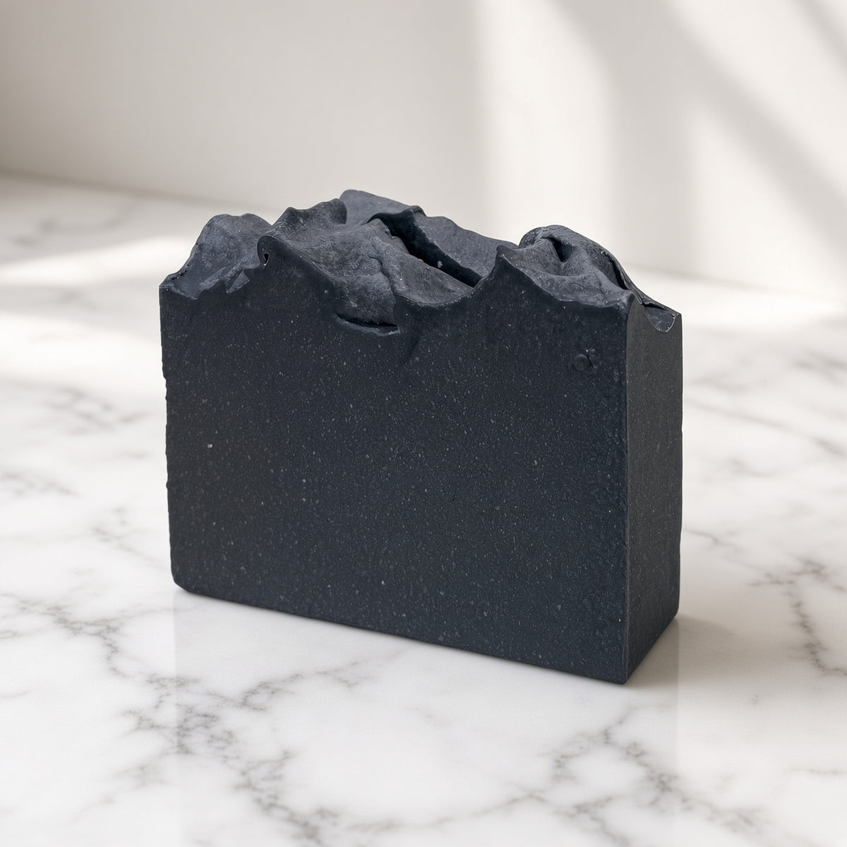 Charcoal goat milk soap bar, matte black with a sculpted wavy top, on white marble