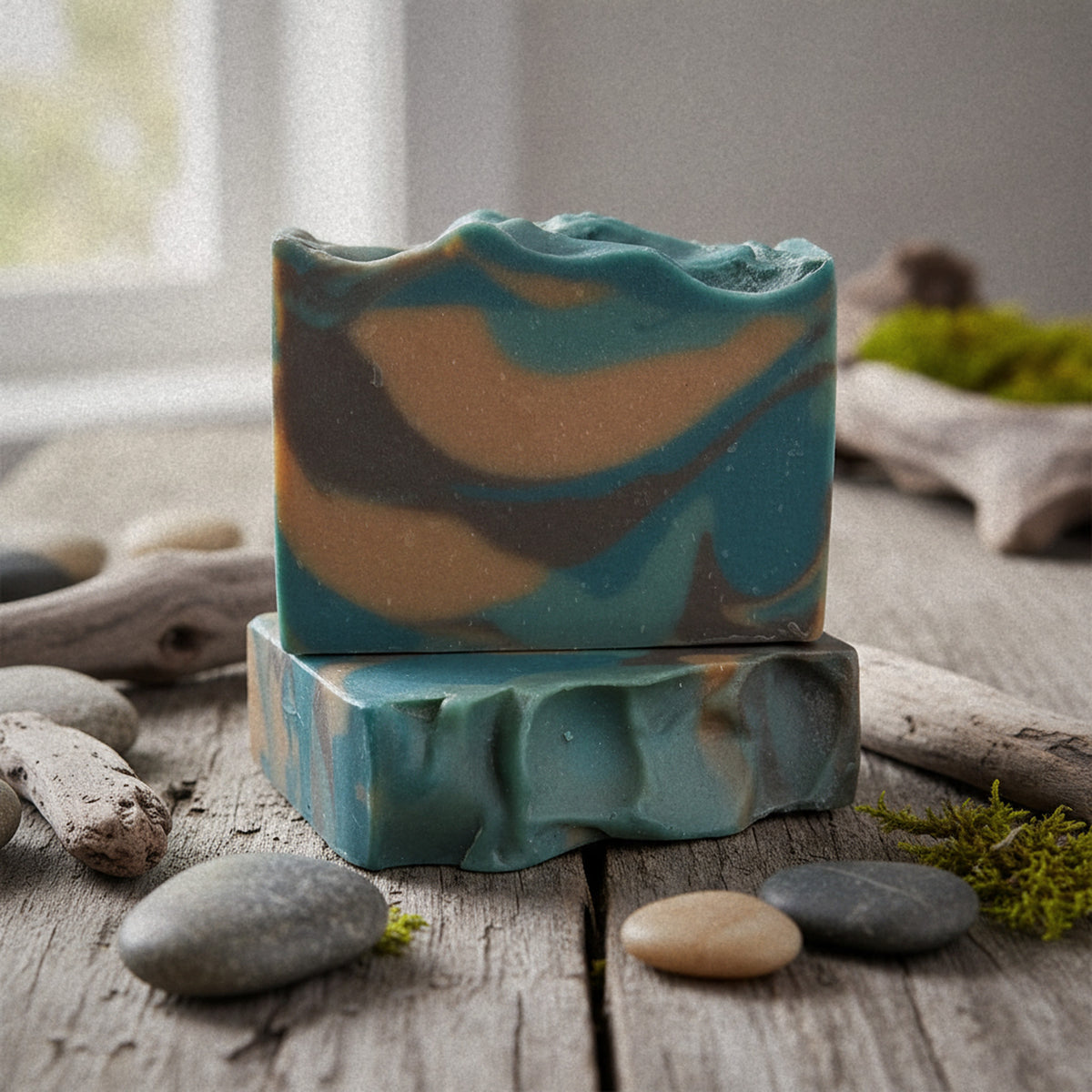 Camo Woods goat milk soap with teal, tan and brown swirls on weathered wood with river stones