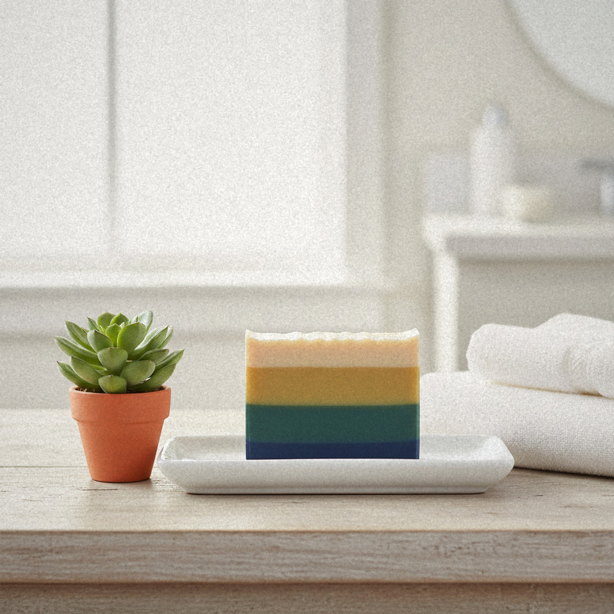 Green Clover & Aloe goat milk soap on a white dish with a potted succulent and towels