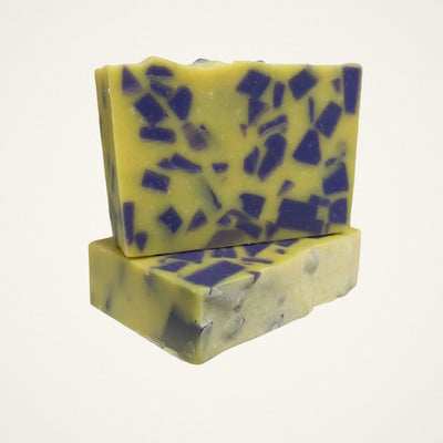 Two Lemon Lavender goat milk soap bars, yellow with purple chunks, on a white background