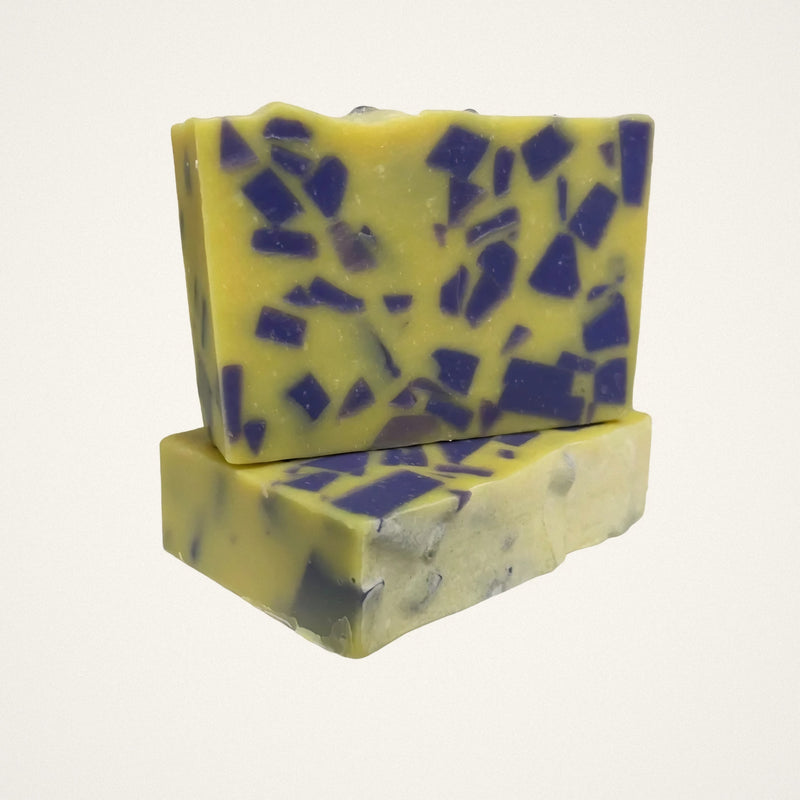 Two Lemon Lavender goat milk soap bars, yellow with purple chunks, on a white background