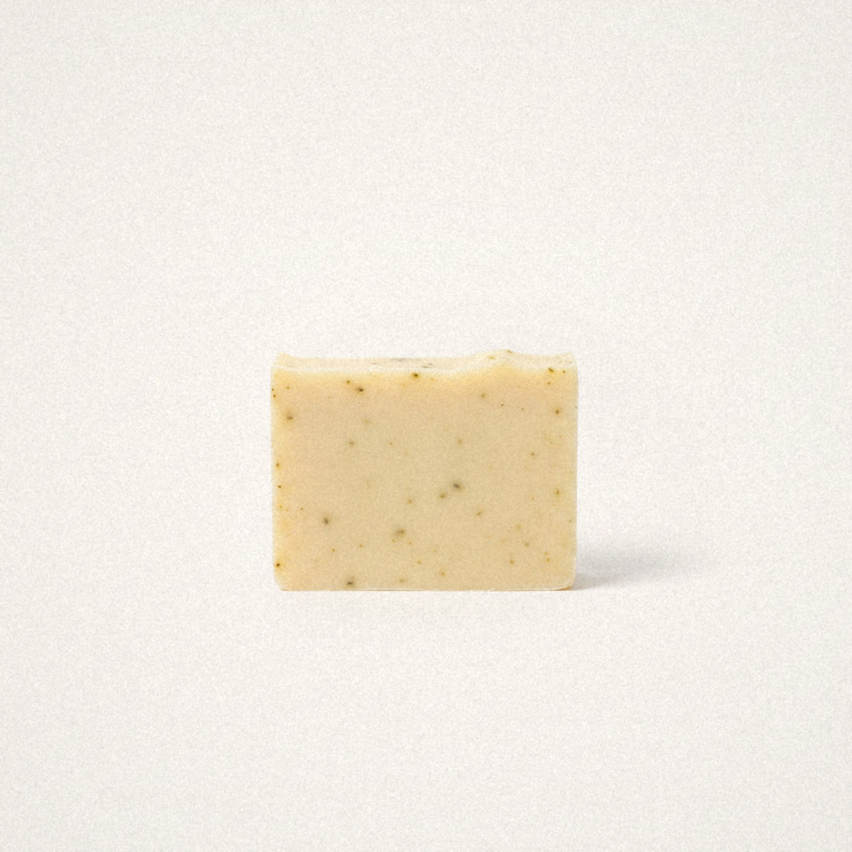 Lemongrass Sage goat milk soap bar, pale yellow with green herb flecks, on a white background
