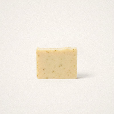 Lemongrass Sage goat milk soap bar, pale yellow with green herb flecks, on a white background