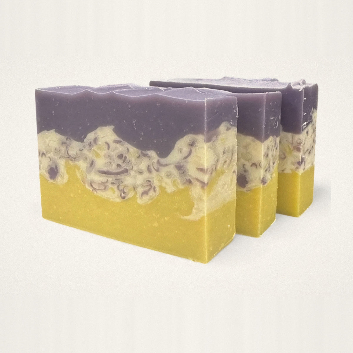 Three Wildberry goat milk soap bars with purple, cream and yellow layers on a white background